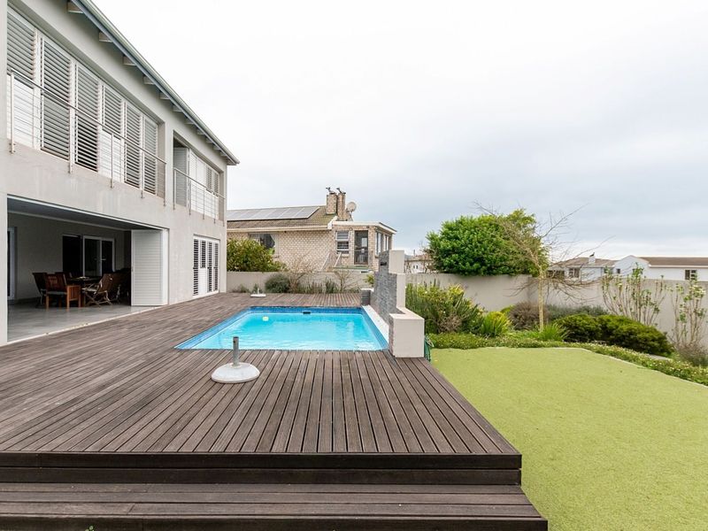 Rear exterior view featuring a timber deck, swimming pool with water feature, and a landscaped garden area adjacent to the main house.