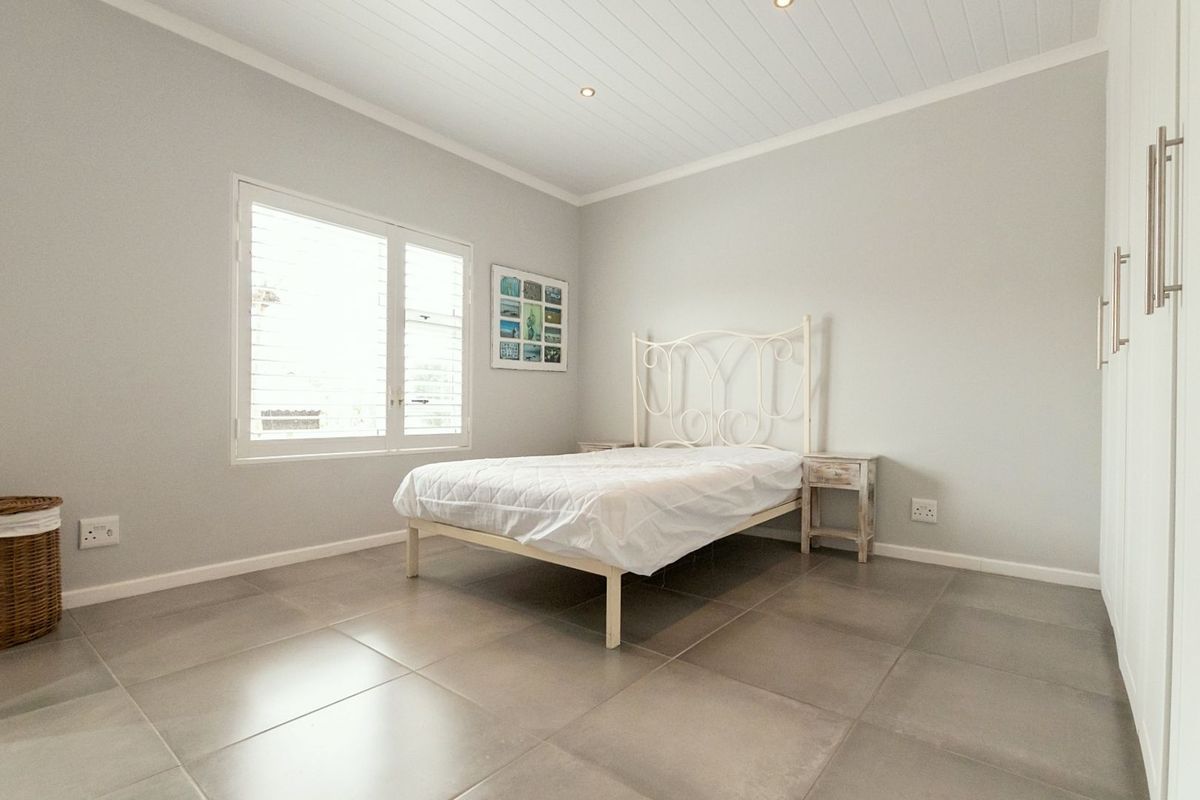 A bright and neutral bedroom featuring large format floor tiles, recessed ceiling lighting, and built-in wardrobe cabinetry.