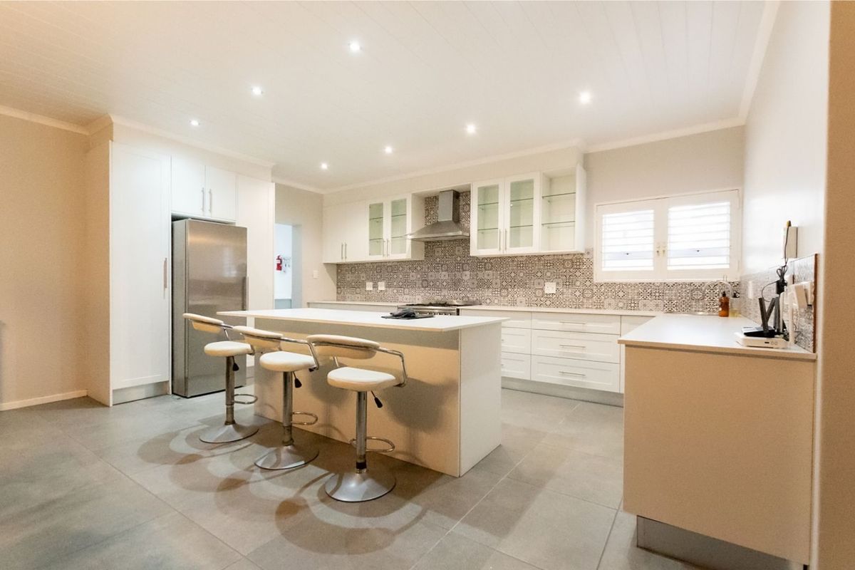 Modern kitchen featuring white cabinetry, a central island with breakfast bar, patterned tile backsplash, stainless steel extractor fan, and large format floor tiles.