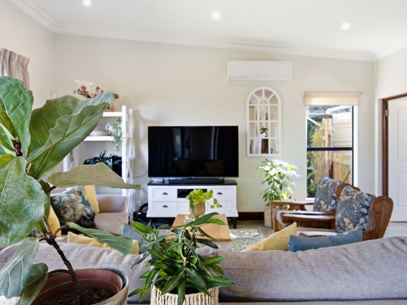 A bright and well-maintained living room featuring recessed downlighting, coving, and a wall-mounted split-system air conditioner.