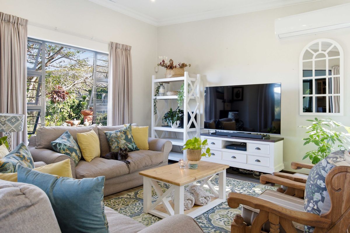 A bright and comfortable living room featuring a large window, split-system air conditioning, and decorative wall detailing.