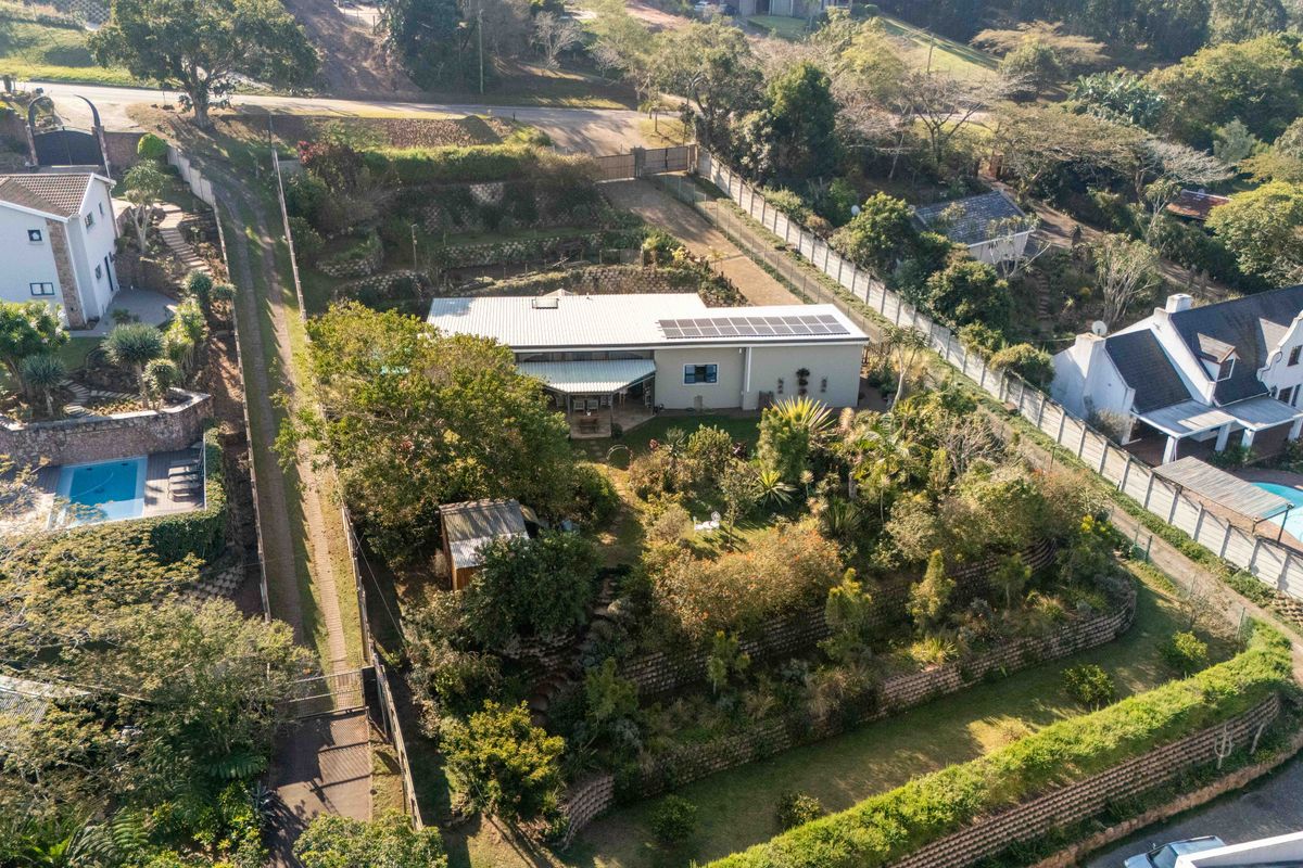 Aerial view of a residential property featuring a metal roof with solar panels, extensive terraced landscaping, and a private driveway.