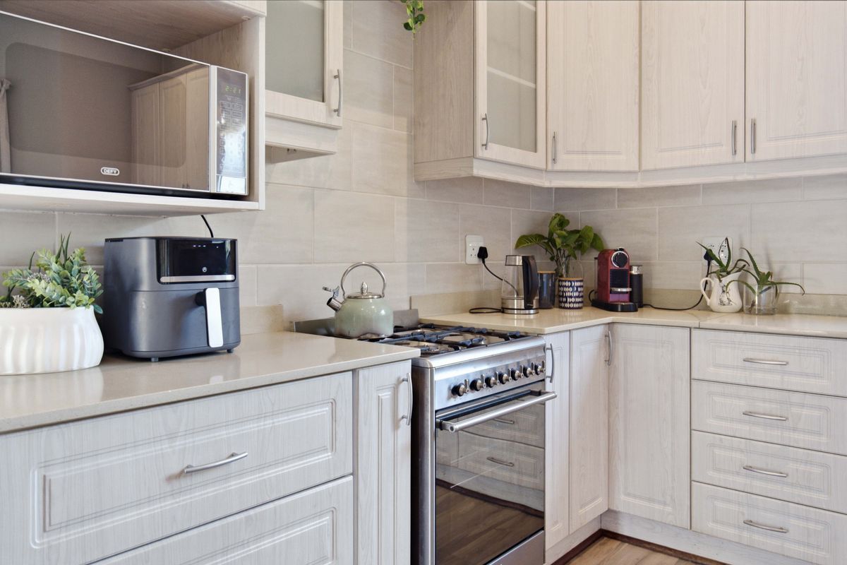 A well-maintained kitchen featuring light wood-grain cabinetry, stone countertops, a tiled backsplash, and a built-in microwave with a gas stove and oven.