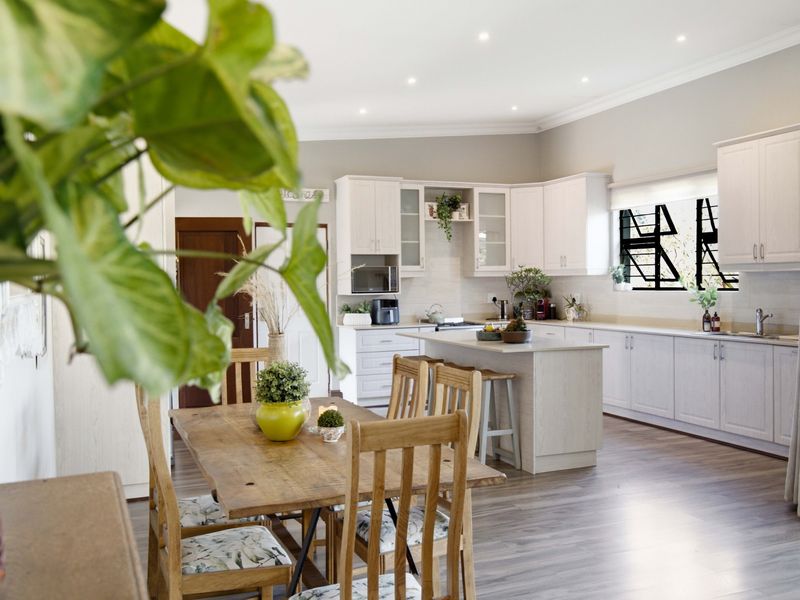 Spacious open-plan kitchen and dining area featuring light-toned cabinetry, a central island, and modern laminate flooring with recessed lighting throughout.