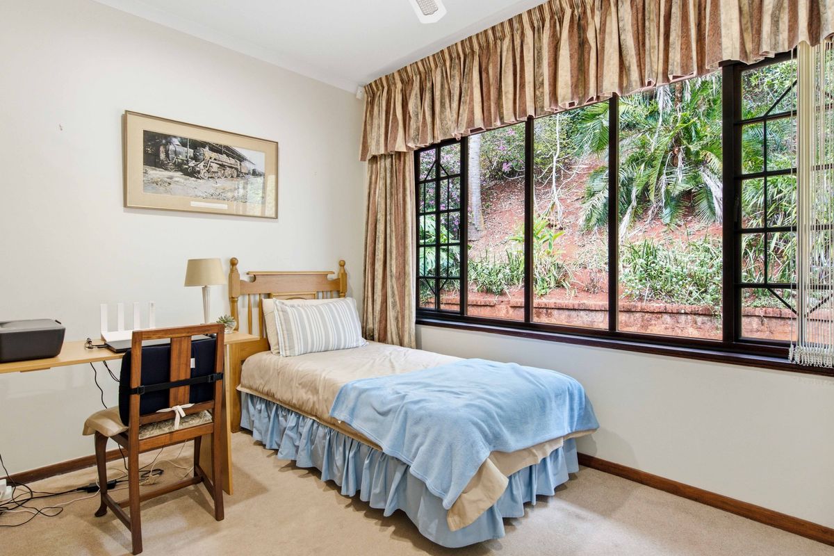 A well-lit bedroom featuring large windows with garden views, neutral wall finishes, and carpeted flooring.