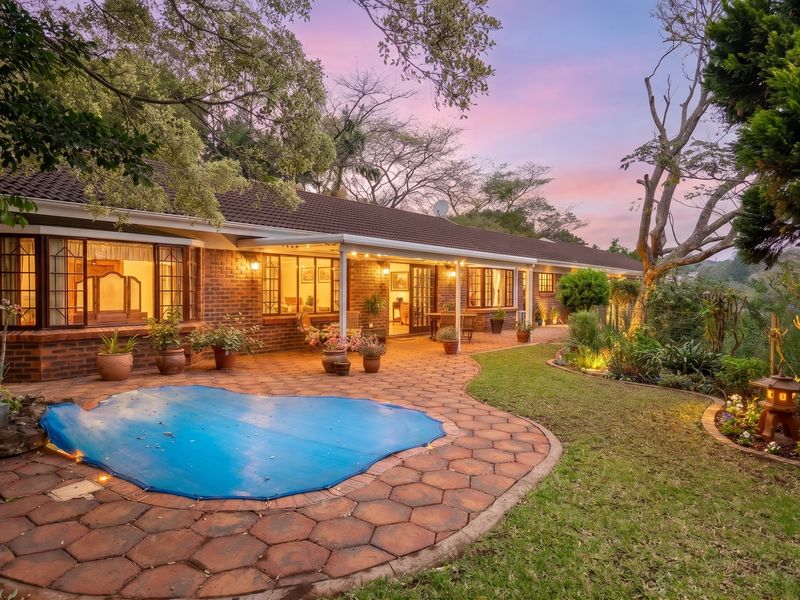 A beautifully landscaped rear exterior featuring a paved patio, swimming pool, and brick facade, perfect for outdoor entertaining in a serene setting.