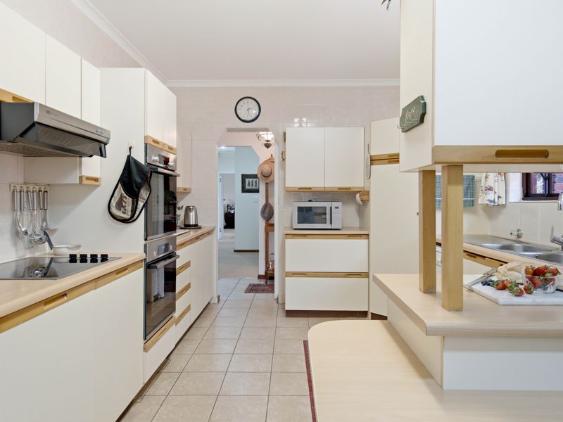 A functional kitchen featuring white cabinetry, laminate countertops, built-in oven, electric cooktop, and tiled flooring, offering a clean and practical workspace.