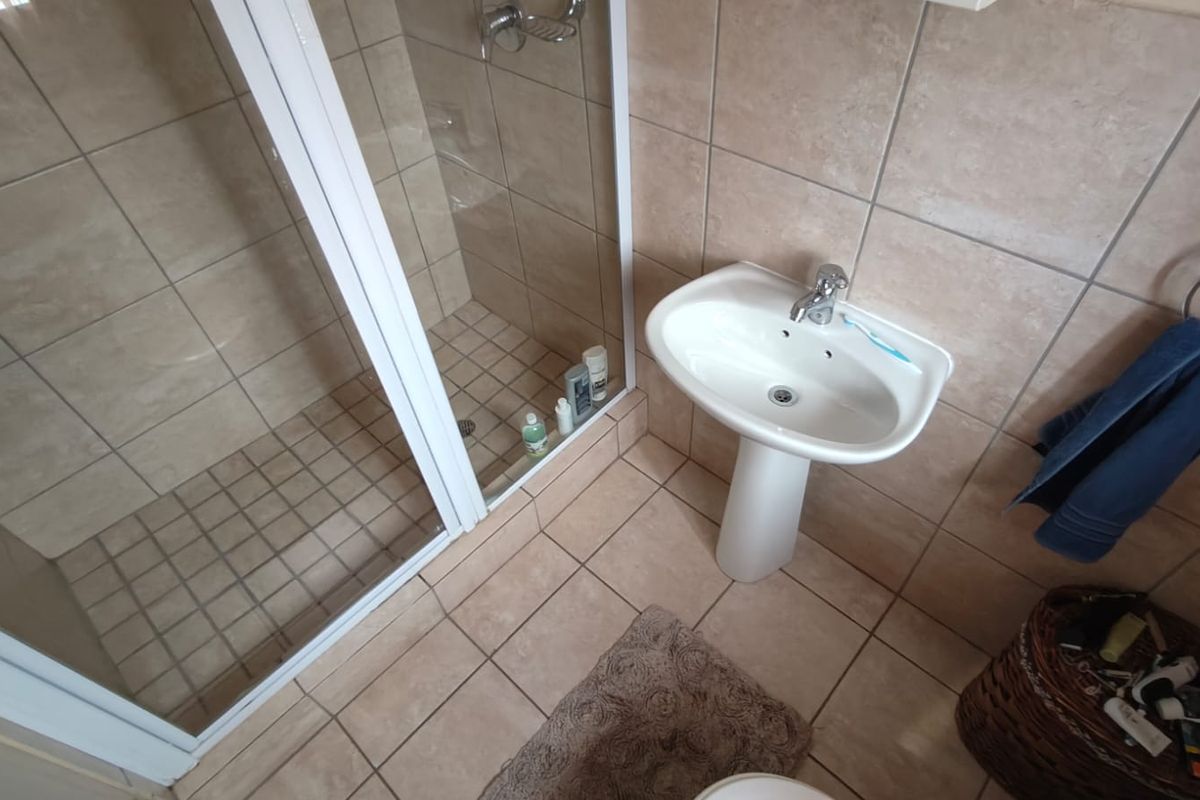 A functional bathroom featuring a pedestal basin, a glass-enclosed shower, and neutral floor-to-ceiling wall tiling.