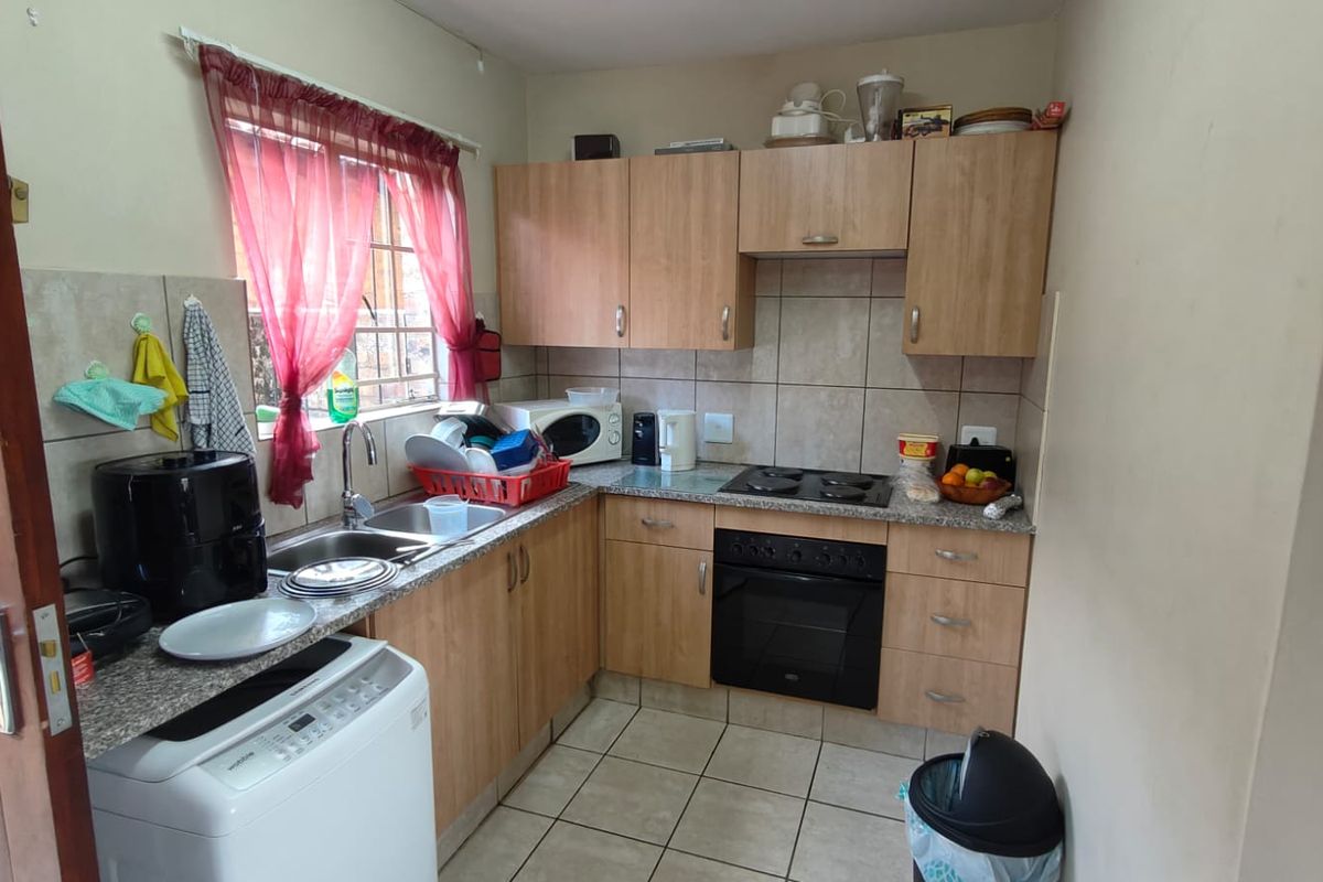 A functional kitchen featuring light wood-finish cabinetry, granite-look countertops, a built-in oven with hob, and tiled flooring.