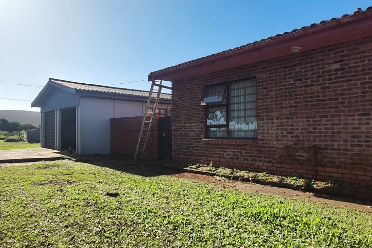 Rear view of the property featuring a brick exterior, tiled roof, and a detached garage with an adjacent concrete driveway and lawn area.