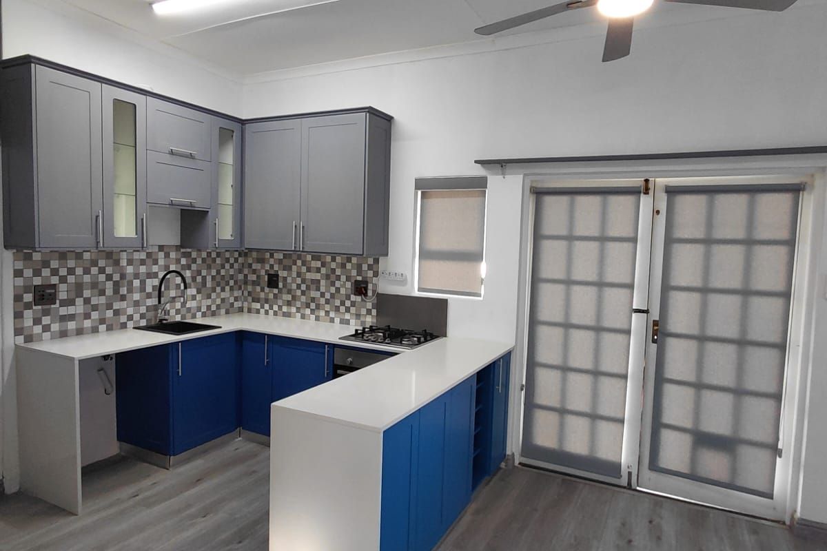 Modern kitchen featuring blue and grey cabinetry, white quartz countertops, gas hob, under-counter oven, and durable laminate flooring with direct access to the patio.