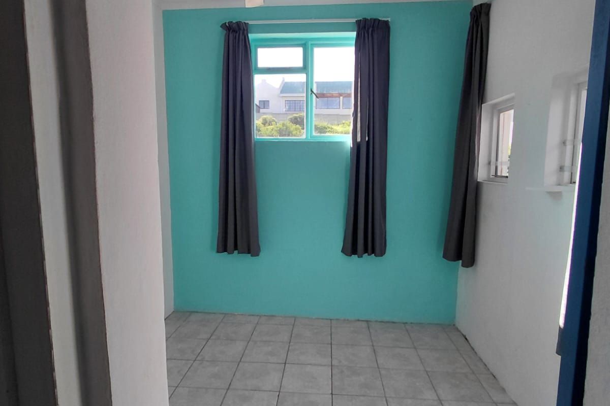 An empty bedroom featuring tiled flooring, a ceiling fan, and bright teal accent wall with aluminium window frames.