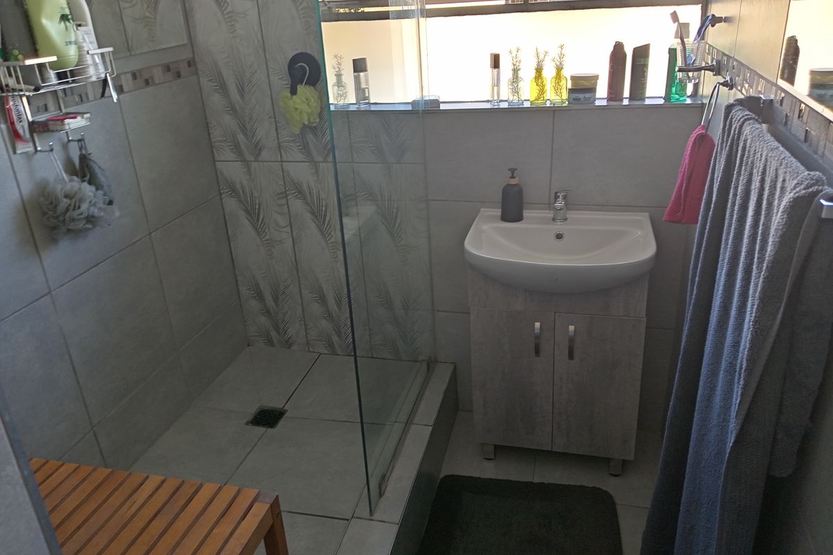 A compact bathroom featuring a glass-enclosed shower, a modern vanity with a basin, and neutral wall tiling.