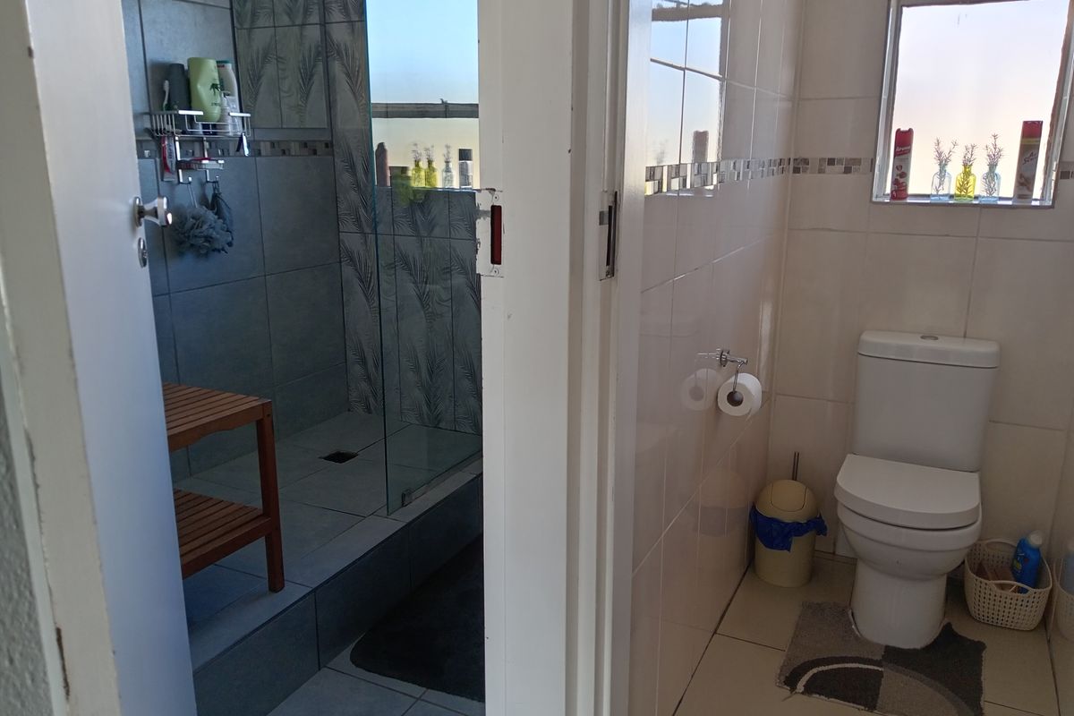A functional bathroom featuring a separate shower enclosure with glass door and a standard toilet, finished with tiled walls and flooring.