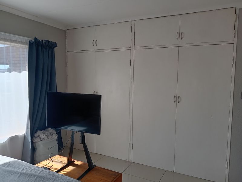 A bedroom featuring built-in floor-to-ceiling cupboards with white cabinetry and tiled flooring.