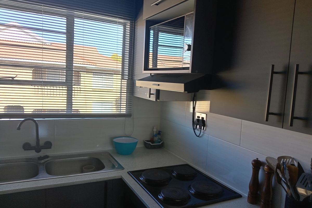 A compact kitchen area featuring a double sink, built-in electric hob, extractor fan, and overhead microwave cabinet with modern dark cabinetry.