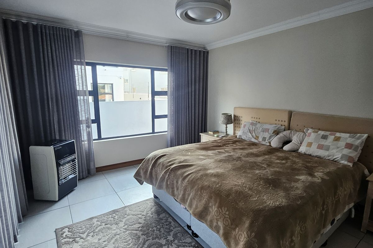 A well-maintained bedroom featuring tiled flooring, a ceiling fan, and large windows with floor-to-ceiling curtains.