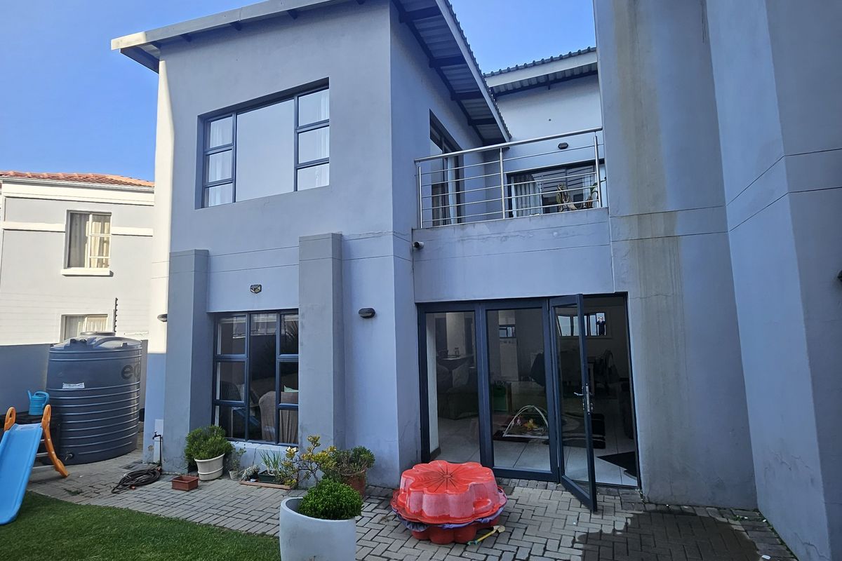 Rear view of the townhouse featuring a paved patio, balcony with stainless steel railing, and aluminium framed windows and doors.
