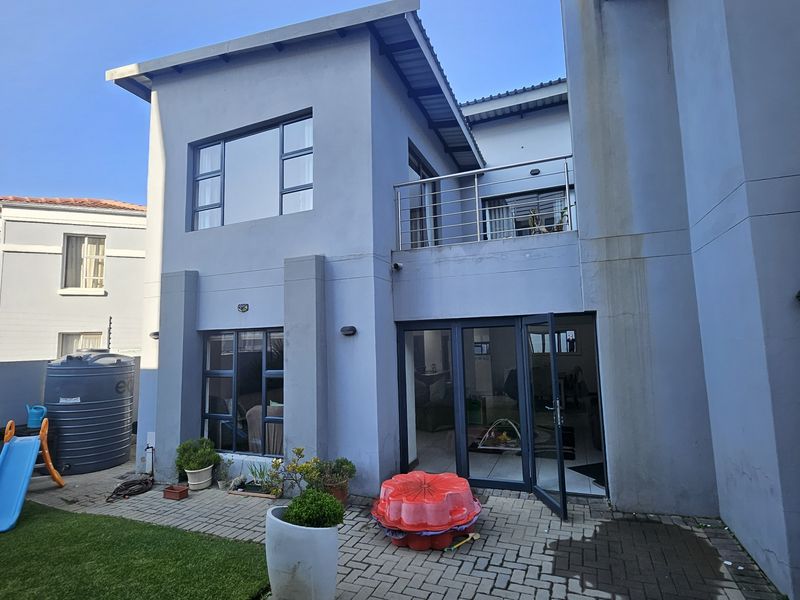 Rear view of the townhouse featuring a paved patio, balcony with stainless steel railing, and aluminium framed windows and doors.