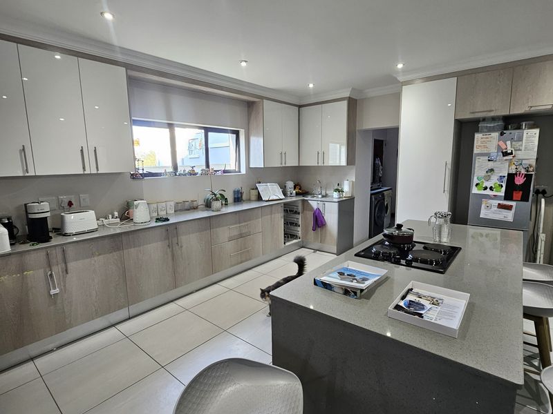 Modern kitchen featuring sleek two-tone cabinetry, stone countertops, a central island with a built-in hob, and large format floor tiles.