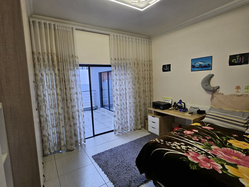 A well-maintained bedroom featuring tiled floors, a modern LED ceiling fixture, and a sliding glass door providing access to an outdoor balcony area.