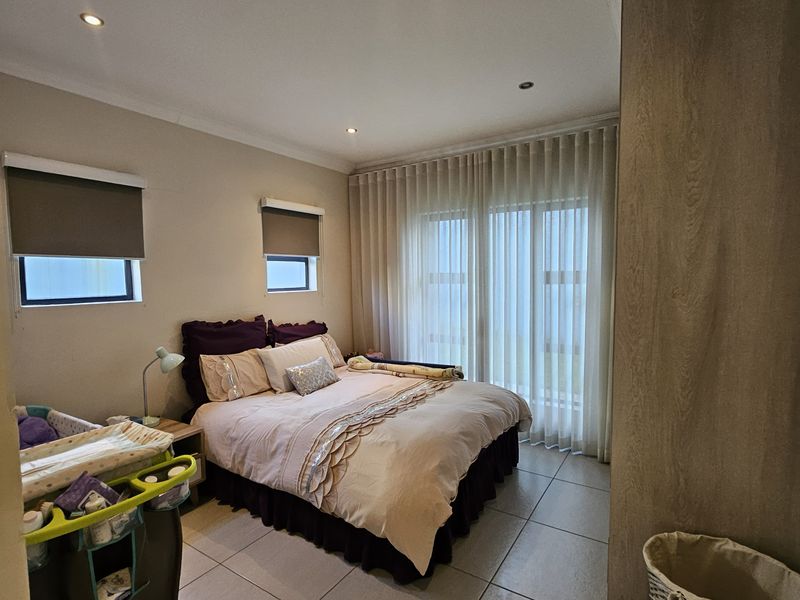 A well-maintained bedroom featuring neutral tiled flooring, recessed downlighting, and floor-to-ceiling sheer curtains providing natural light control.