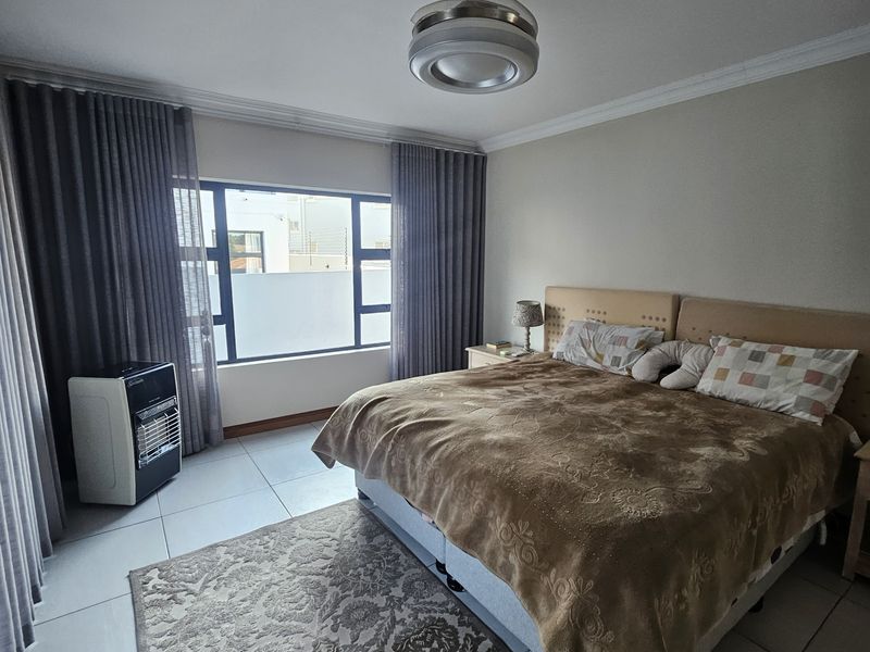 A well-maintained bedroom featuring tiled flooring, a ceiling fan, and large windows with floor-to-ceiling curtains.