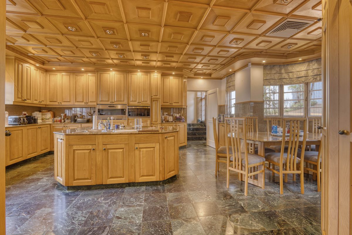 Spacious kitchen featuring extensive light wood cabinetry, a central island, granite countertops, and a distinctive coffered wood ceiling with integrated lighting.