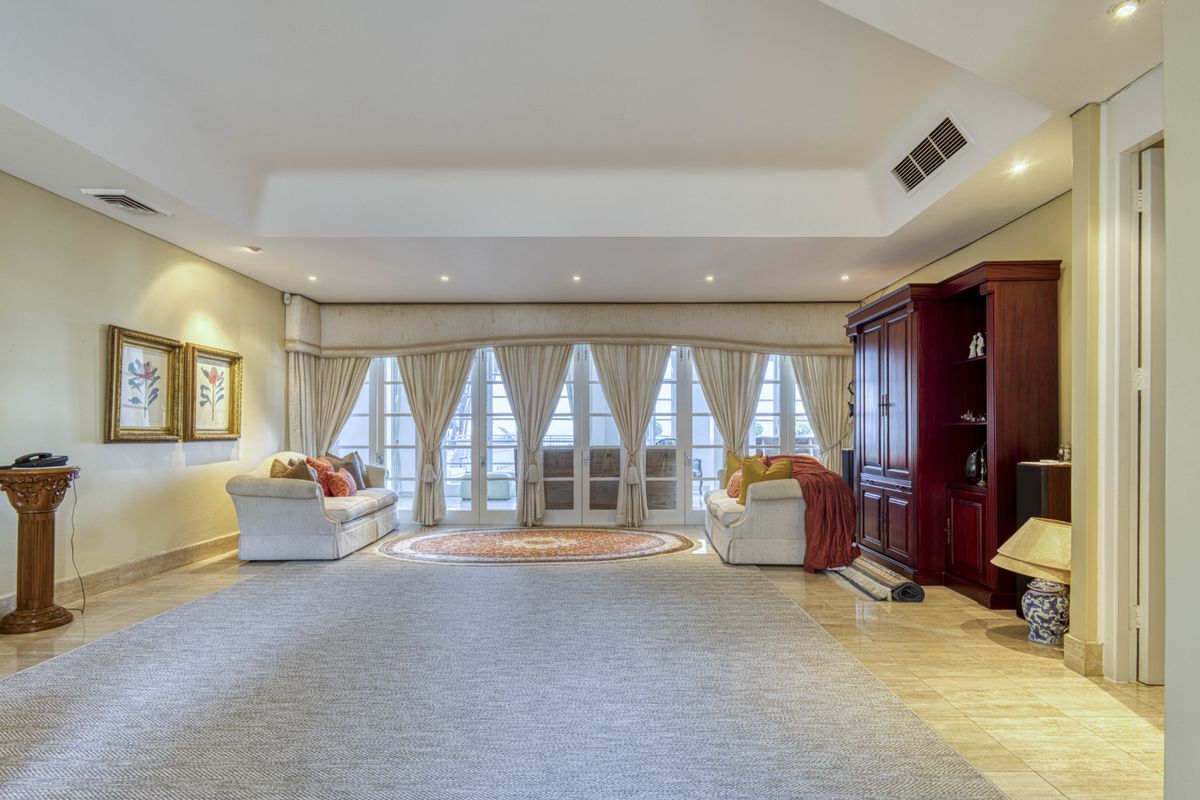 Spacious living room featuring a tray ceiling, recessed lighting, ducted air conditioning, and large glass-paned double doors leading to an outdoor area.
