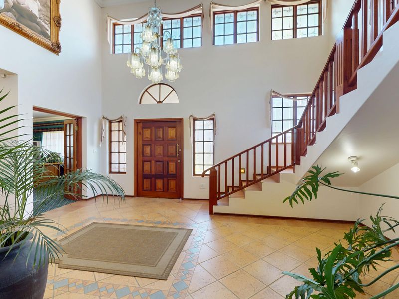 Spacious double-volume entrance hall featuring a grand timber staircase, tiled flooring, and a feature chandelier, creating an impressive and welcoming foyer.