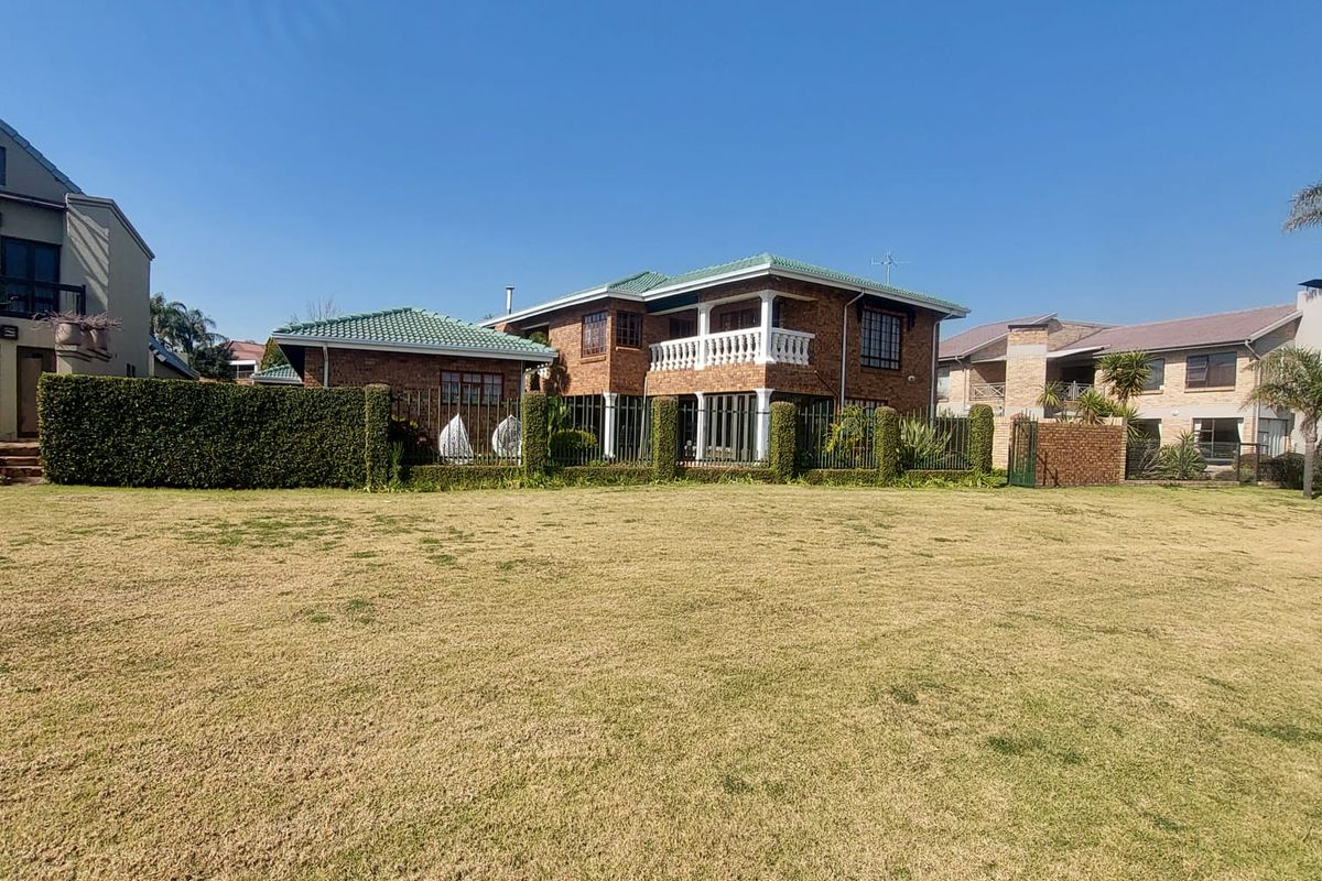 A view of the rear elevation of a two-story brick house featuring a tiled roof, upper-level balcony, and a large grassed garden area.