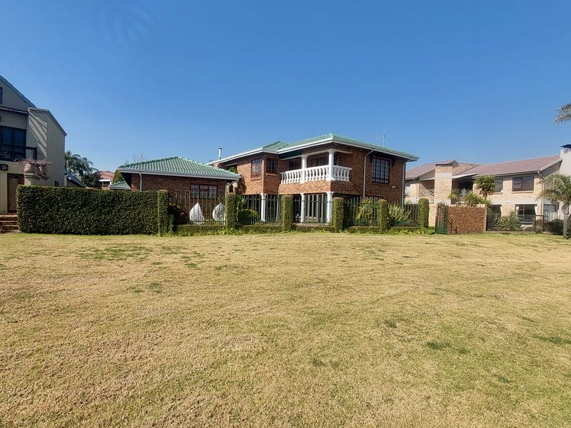 A view of the rear elevation of a two-story brick house featuring a tiled roof, upper-level balcony, and a large grassed garden area.