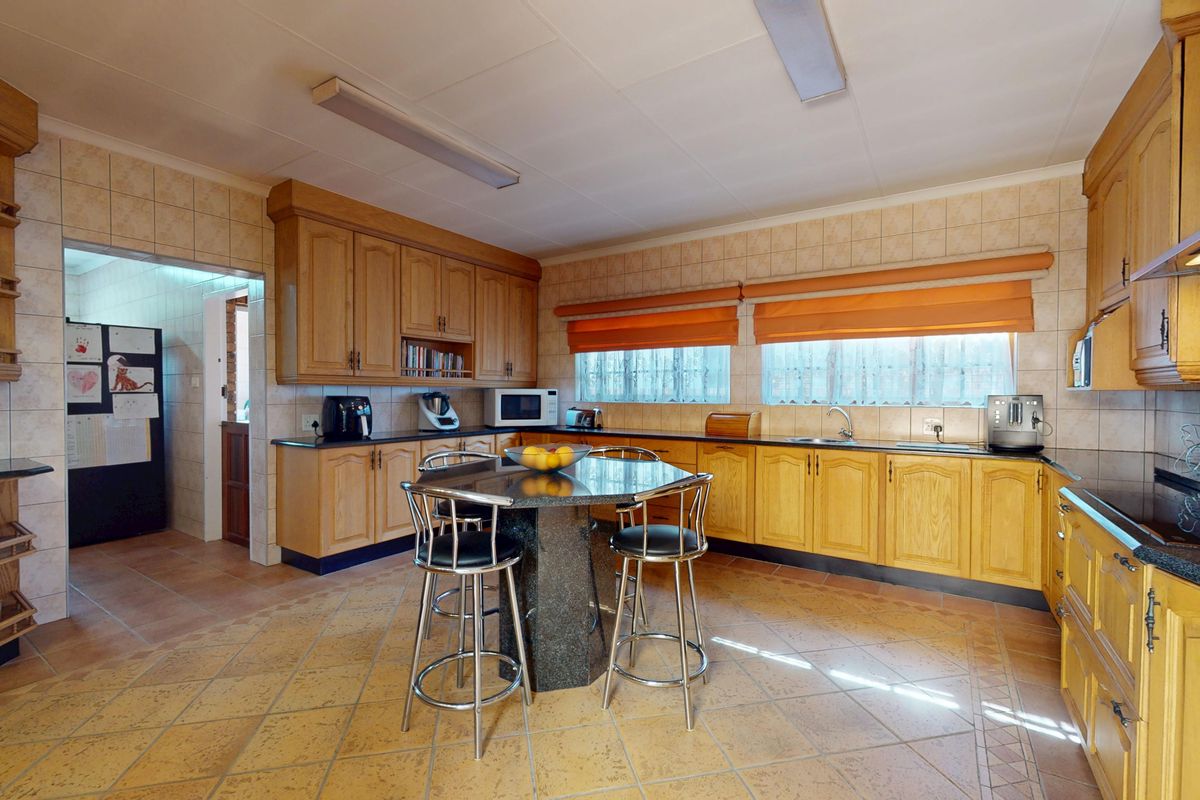 Spacious kitchen featuring extensive wooden cabinetry, granite countertops, tiled flooring, and a central breakfast island with integrated seating.