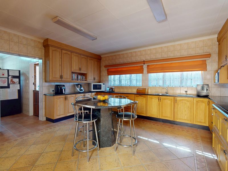 Spacious kitchen featuring extensive wooden cabinetry, granite countertops, tiled flooring, and a central breakfast island with integrated seating.