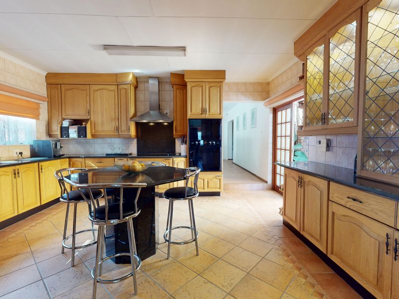 Spacious kitchen featuring traditional wooden cabinetry, granite countertops, built-in oven, stainless steel extractor fan, and tiled flooring with a central breakfast island.