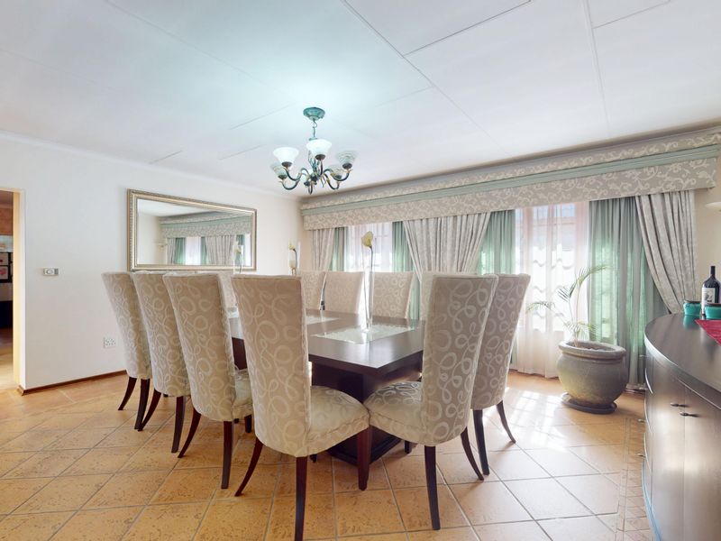 A spacious dining room featuring tiled flooring and a classic chandelier, with an adjacent view into the kitchen area.