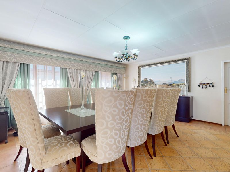A spacious dining room featuring tiled flooring, a decorative ceiling light fixture, and a large window with a pelmet.