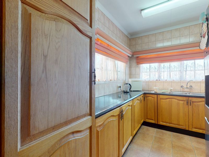 A functional kitchen featuring traditional wooden cabinetry, granite countertops, tiled backsplash, and a stainless steel sink with ample natural light.