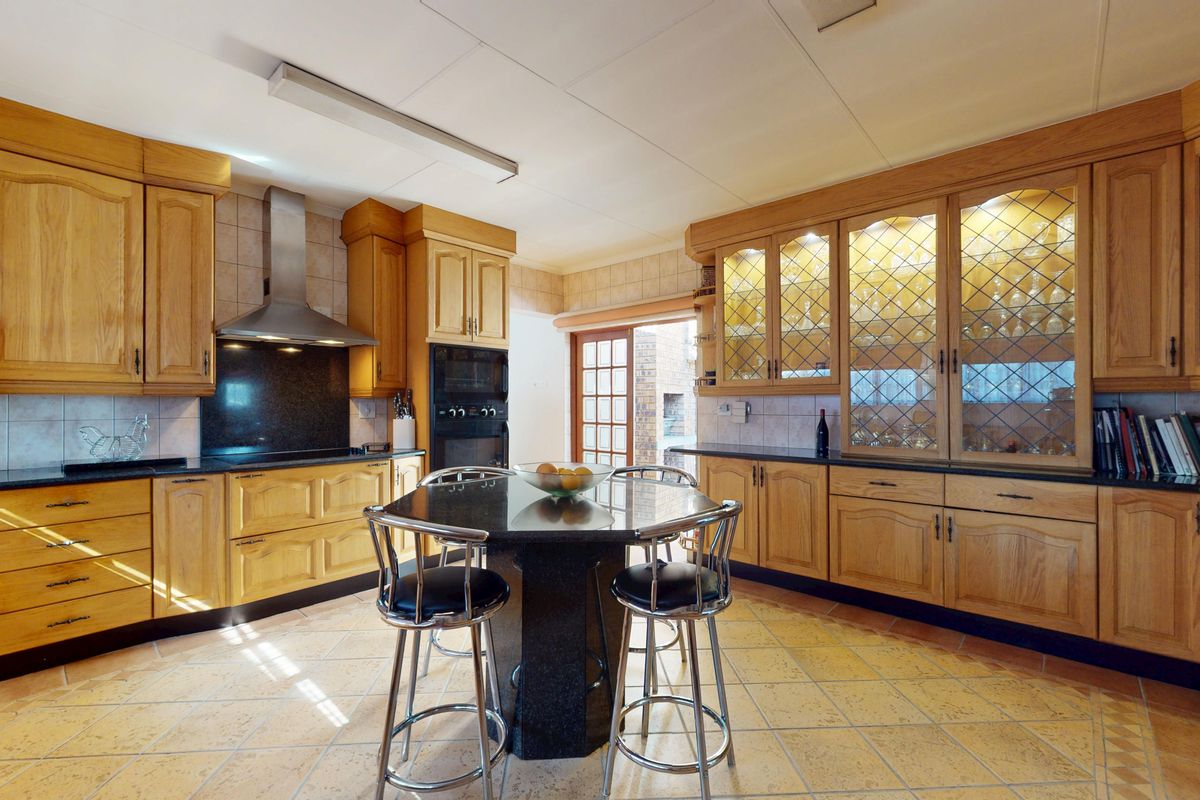 Spacious kitchen featuring traditional wooden cabinetry, granite countertops, built-in oven, extractor fan, and glass-fronted display cabinets with tiled flooring.