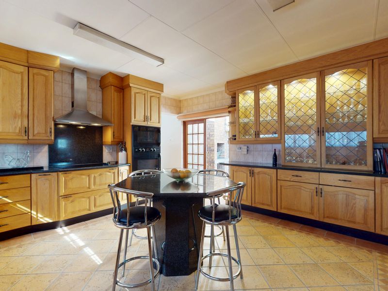 Spacious kitchen featuring traditional wooden cabinetry, granite countertops, built-in oven, extractor fan, and glass-fronted display cabinets with tiled flooring.