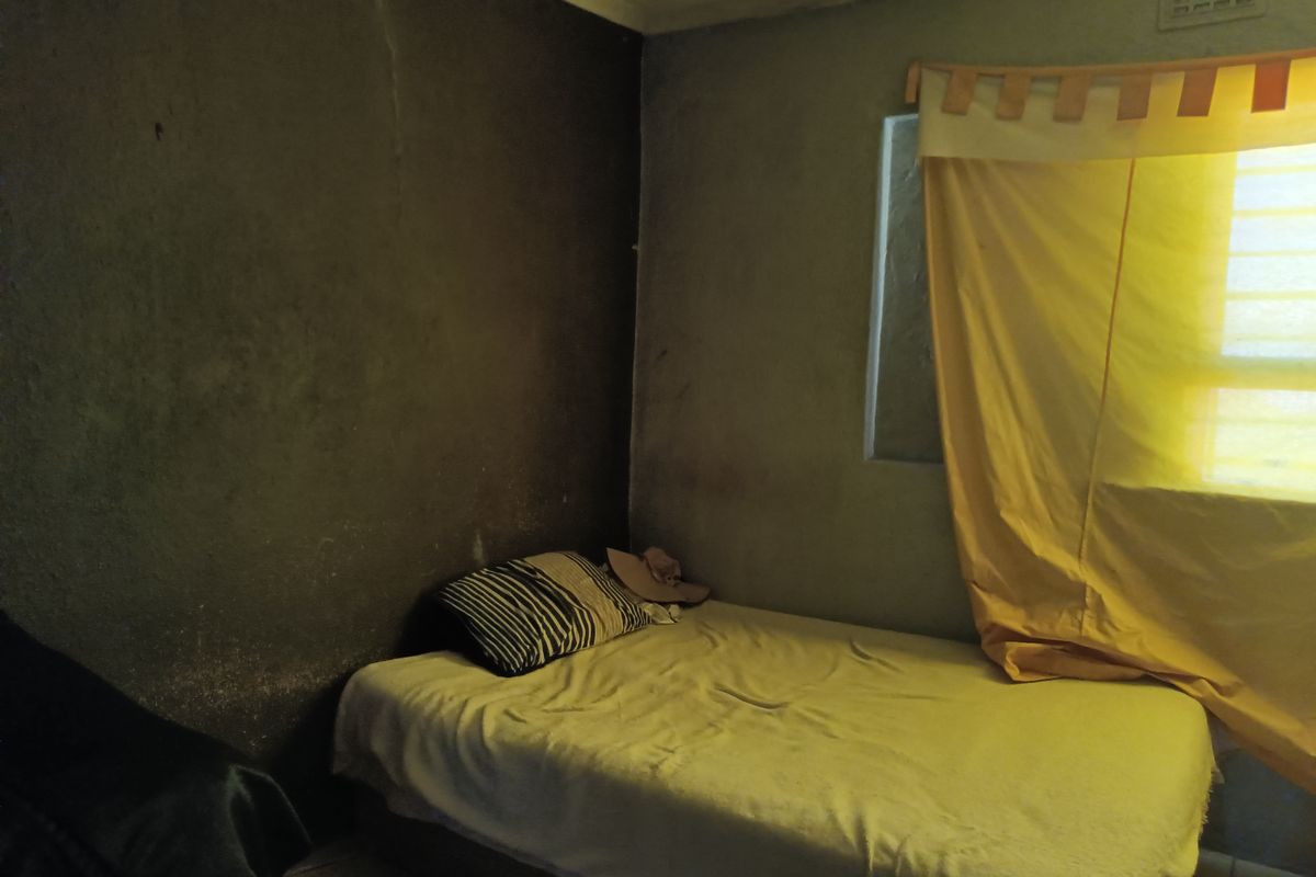 A bedroom featuring basic wall finishes and a ceiling vent, requiring cosmetic updates and improved lighting to enhance the living space.