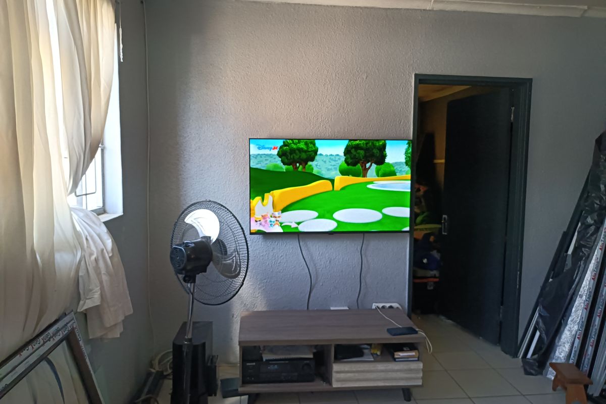 A living room area featuring tiled flooring and a wall-mounted television, providing a functional space for entertainment.