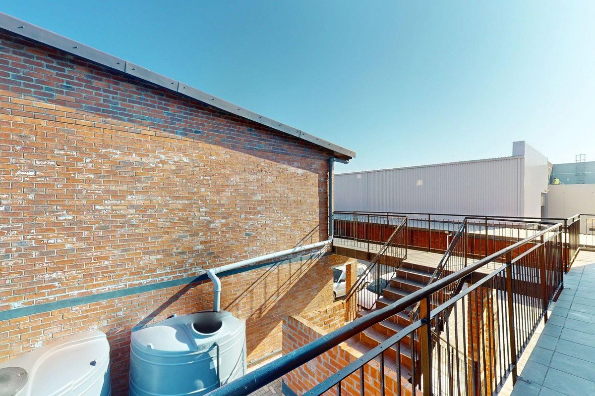 Exterior view of an apartment building featuring a brick facade, metal staircase, and balcony area with a water storage tank.
