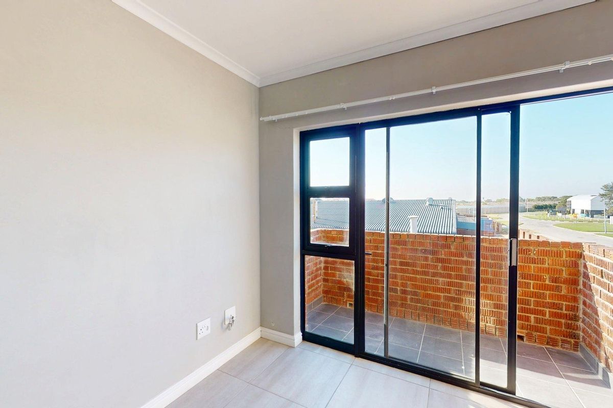 A bright, empty bedroom featuring neutral walls, tiled flooring, and a sliding glass door providing access to a private balcony.