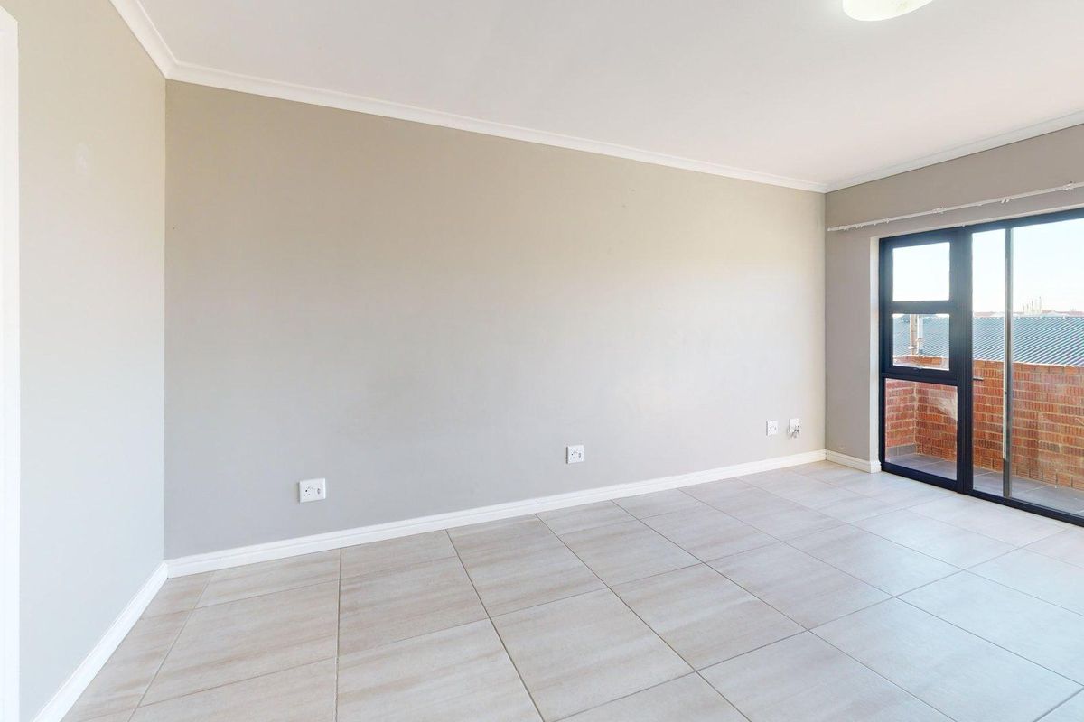 A bright, empty living room featuring neutral tiled flooring, clean walls, and a sliding glass door providing access to an outdoor balcony area.