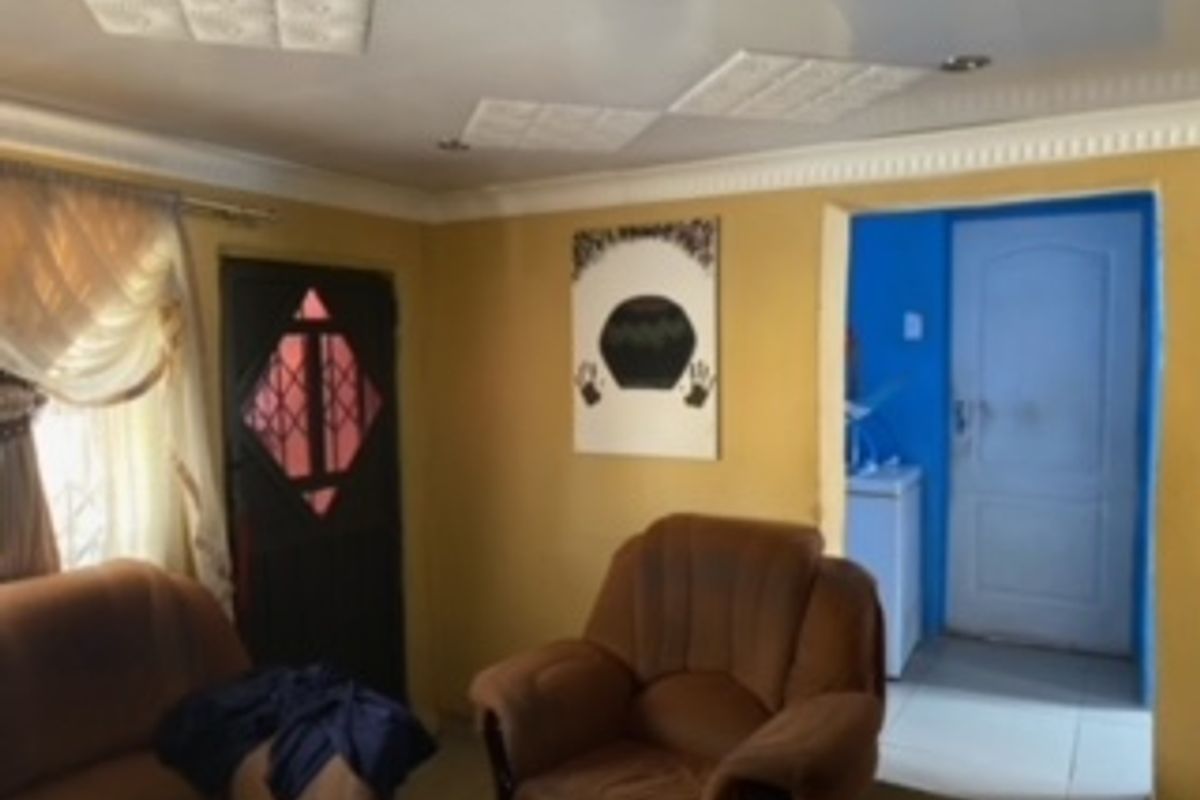 Living room area featuring decorative ceiling tiles, coved cornicing, and a security gate, leading through to an adjacent room.