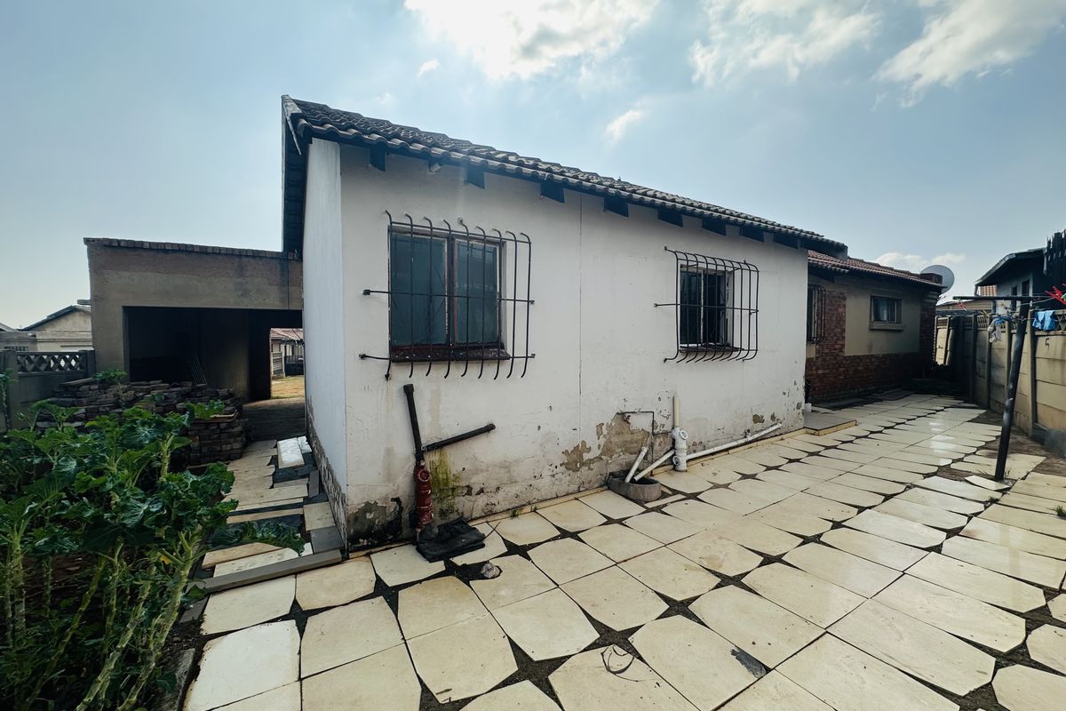 Rear exterior view of the property featuring a tiled patio area, security bars on windows, and visible exterior wall maintenance requirements.
