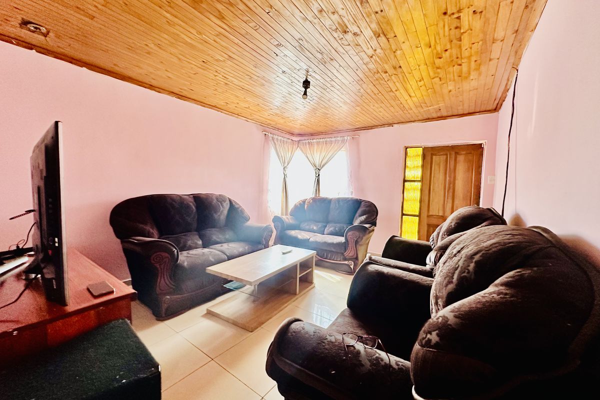 A living room featuring a timber tongue and groove ceiling, tiled flooring, and a wooden door with glass panels.