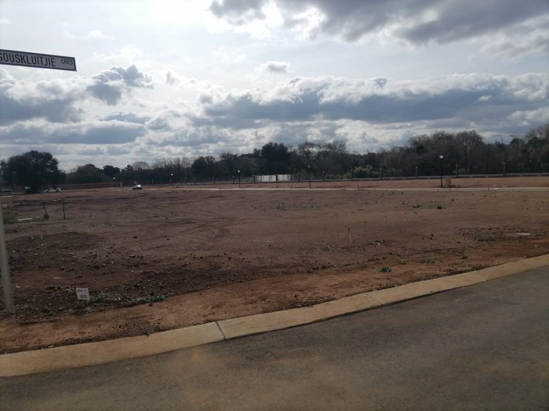 A vacant residential plot of land featuring a paved curb, boundary wall, and street signage, ready for development.