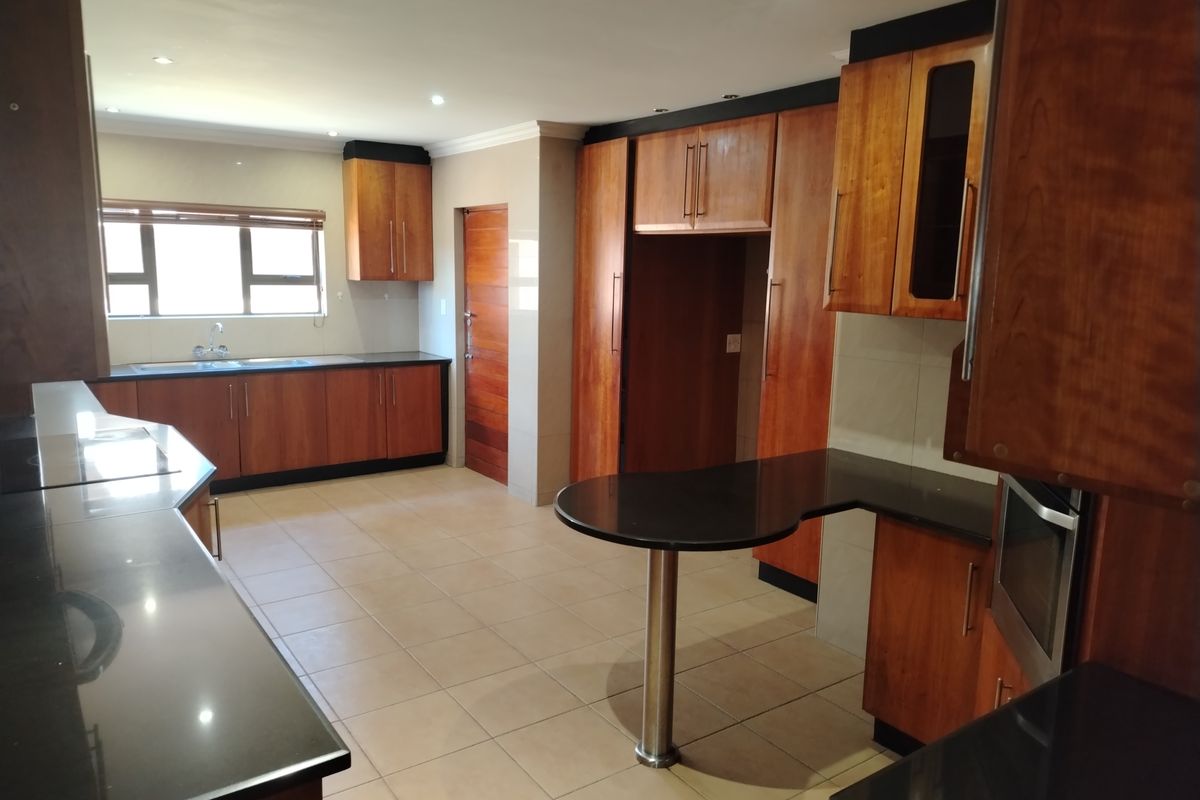 Spacious kitchen featuring dark granite countertops, warm wood cabinetry, integrated oven, and a breakfast bar island with tiled flooring.